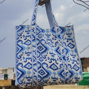 K&ouml;nnte beinhalten: Eine gro&szlig;e Tragetasche mit einem blau-wei&szlig;en geometrischen Muster. Die Tasche hat zwei Griffe und ist aus einem strukturierten Stoff gefertigt. Das Design zeigt sich wiederholende Formen und Linien.