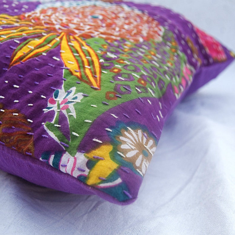 May include: Purple and green kantha throw pillow with a floral pattern. The pillow is made of recycled saris and has a unique hand-stitched design.