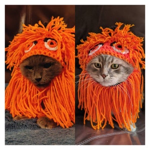Puede incluir: Dos gatos con sombreros de ganchillo naranja con una melena naranja peluda. Los sombreros tienen un diseño de ganchillo blanco y rojo. Los gatos miran a la cámara.