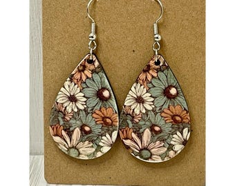 May include: Teardrop-shaped earrings with a floral pattern. The earrings feature a wooden base with a design of white, orange, and blue flowers. The earrings have silver-colored hooks.