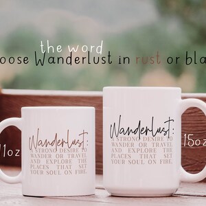 May include: Two white ceramic mugs with the word "Wanderlust" in black script and a definition of the word in rust colored text. The mugs are 11 oz and 15 oz.