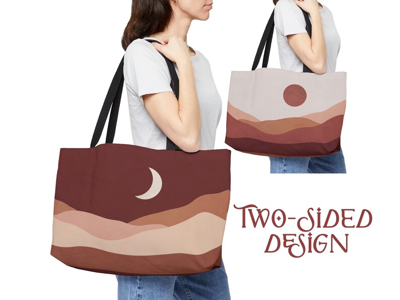 May include: Two-sided tote bag featuring a minimalist landscape design. One side displays a crescent moon over layered brown hills, the other a sun over similar hills. The bag has black straps and the text "TWO-SIDED DESIGN".
