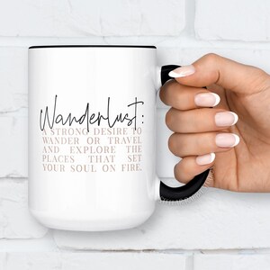May include: White ceramic mug with a black rim and handle. The mug has a black and white graphic that says "Wanderlust: A strong desire to wander or travel and explore the places that set your soul on fire."