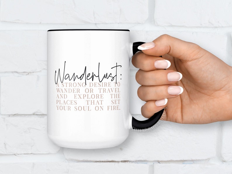 May include: White ceramic mug with a black rim and handle. The mug has a black and white graphic that says "Wanderlust: A strong desire to wander or travel and explore the places that set your soul on fire."