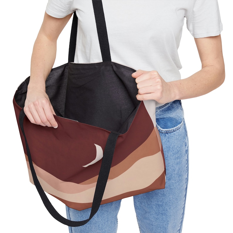 May include: A large tote bag with a brown, tan, and beige abstract design. The bag has black straps and a black interior. The bag is being held open, revealing the interior.