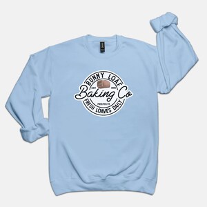 May include: Light blue long-sleeved sweatshirt with a white circle logo that says "Bunny Loaf Baking Co. Est. 1982 Fresh Premium Loaves Daily".