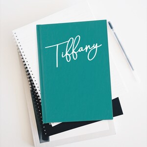 May include: A teal notebook with the name "Tiffany" written in white cursive on the front cover.