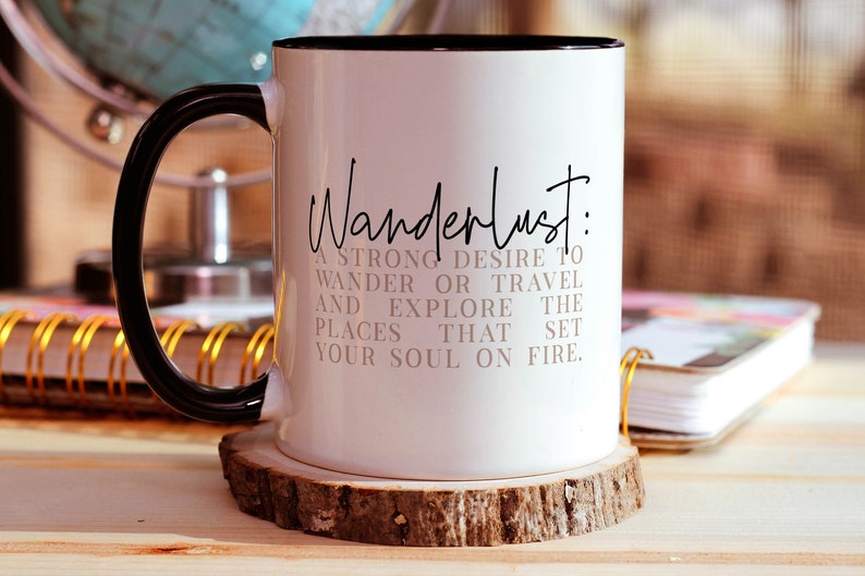 May include: White ceramic mug with a black handle and black rim. The mug has the text "Wanderlust: A strong desire to wander or travel and explore the places that set your soul on fire." printed in black.