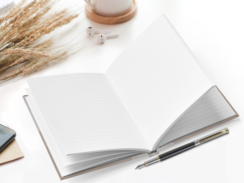 Pu&ograve; includere: Un quaderno a copertina rigida aperto con una penna d'argento su una superficie bianca. Il quaderno &egrave; aperto su una pagina bianca e la penna &egrave; appoggiata sul quaderno.