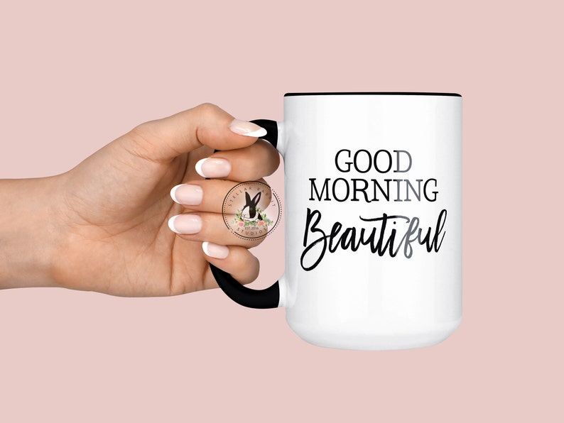 Peut inclure: Une tasse en c&eacute;ramique blanche avec un bord et une poign&eacute;e noirs. La tasse porte l'inscription noire "Good Morning Beautiful".
