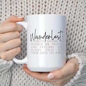 May include: White ceramic mug with a black and pink design. The mug features the text "Wanderlust: A strong desire to wander or travel and explore the places that set your soul on fire."