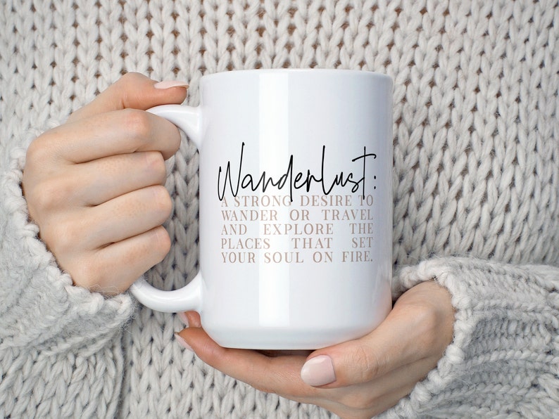 May include: White ceramic mug with a black and pink design. The mug features the text "Wanderlust: A strong desire to wander or travel and explore the places that set your soul on fire."