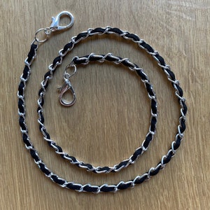 May include: A black and silver chain with a silver clasp. The chain is made of two strands, one black and one silver, that are intertwined.
