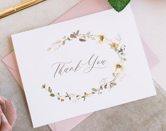 May include: A white thank you card with a floral wreath design in shades of brown, yellow, and green. The text "Thank You" is written in cursive script.