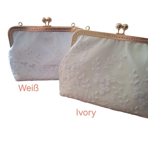 Zwei elfenbein- und weiße Clutch  mit floraler Stickerei. Die Taschen haben einen Kiss-Lock-Verschluss mit einem goldfarbenen Rahmen. Die linke Geldbörse ist mit "Weiß" und die rechte mit "Ivory" beschriftet.