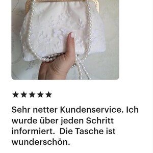Kundenbewertung - Weiße Spitzentasche mit goldenem Verschluss und Perlenriemen. Die Tasche hat zarte Blumenstickereien. Das Bild enthält deutschen Text, der den Kundenservice und die Schönheit der Tasche lobt.