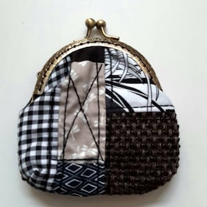 Könnte beinhalten: Eine kleine Patchwork-Münzbörse mit einem Messingverschluss. Die Börse besteht aus verschiedenen Stoffen, darunter schwarz-weißes Gingham, braunes gewebtes Gewebe und ein beigefarbener Stoff mit einem Libellenmuster.