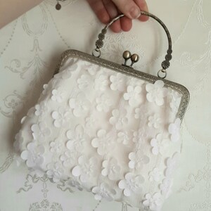 May include: A white clutch purse with a silver frame and a floral design. The purse has a top handle.