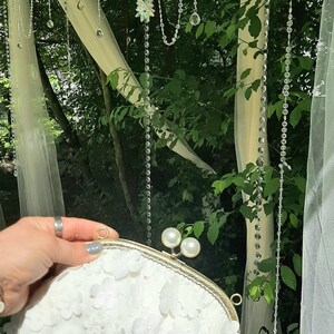 May include: A white clutch purse with a floral design and a gold clasp. The purse is decorated with pearl-like embellishments.
