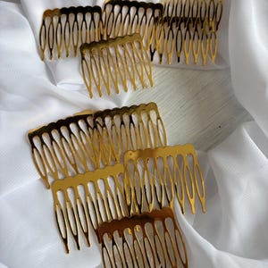Könnte beinhalten: Eine Ansammlung von goldfarbenen Haarkämmen aus Metall, die jeweils eine Reihe schlanker, gebogener Zinken und eine glatte, gewellte Oberkante aufweisen. Diese Haaraccessoires sind in einer Gruppe angeordnet und zeigen ihre reflektierende Oberfläche.