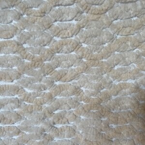 May include: Close-up of a textured, off-white fabric with a pattern of raised, rounded shapes. The fabric has a slightly worn appearance with some loose fibers.