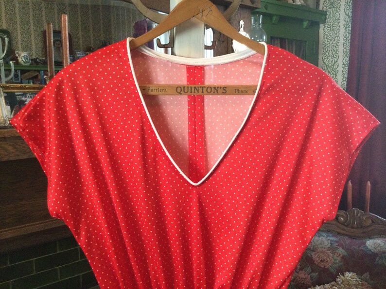 May include: Red sleeveless dress with white polka dots and a white trim around the neckline. The dress is hanging on a wooden hanger. The tag on the hanger reads "Quinton's Phone".