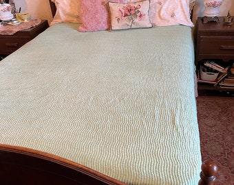 Puede incluir: Una cama con un marco de madera, un edredón acolchado verde y almohadas con estampado floral. La cama está en un dormitorio con una mesita de noche a cada lado.