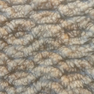 May include: Close-up of a white and beige textured fabric with a raised pattern. The fabric has a soft, fuzzy texture.