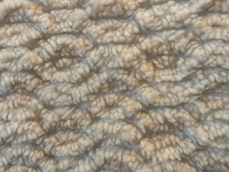 May include: Close-up of a white and beige textured fabric with a raised pattern. The fabric has a soft, fuzzy texture.