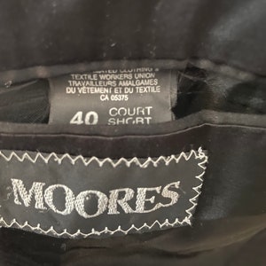 Puede incluir: Una etiqueta negra con texto blanco que dice "MIER CUIMING TEXTILE WORKERS UNION TRAVAILLEURS AMALGAMES DU V&Ecirc;TEMENT ET DU TEXTILE CA 05375 COURT 40 SHORT" y una etiqueta negra con costuras blancas que dice "MOORES".