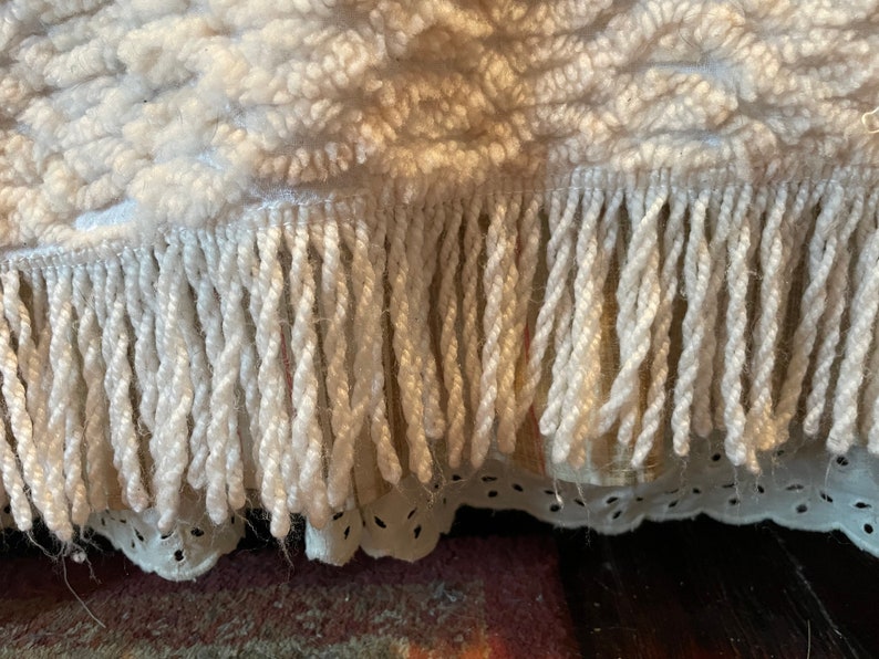 May include: Close-up of a white woven rug with a fringe border. The fringe is made of twisted yarn.