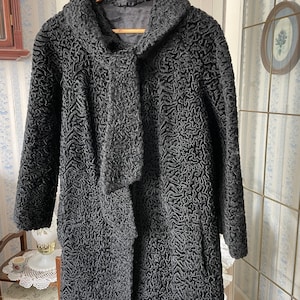 Peut inclure: Un manteau en fourrure bouclée noire avec un col châle. Le manteau est suspendu à un cintre en bois.