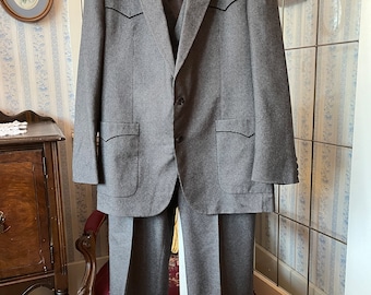 Puede incluir: Una chaqueta de traje gris de rayas finas y pantalones a juego. La chaqueta tiene solapa de muesca, dos bolsillos de solapa y cierre de un botón. Los pantalones tienen pierna recta.