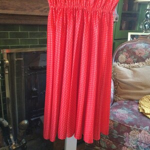 May include: A red skirt with white polka dots. The skirt is made of a lightweight fabric and has a gathered waist.
