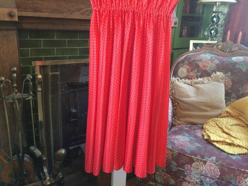 May include: A red skirt with white polka dots. The skirt is made of a lightweight fabric and has a gathered waist.