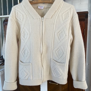 May include: A cream knitted cardigan with a zip fastening and two pockets. The cardigan features a diamond pattern and the label reads "All Wool 38".