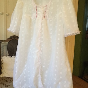 May include: A white sheer nightgown with a pink floral pattern and lace trim. The gown has a V-neckline and short sleeves.