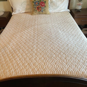 May include: A white tufted bedspread with a floral patterned pillow on a wooden bed frame.