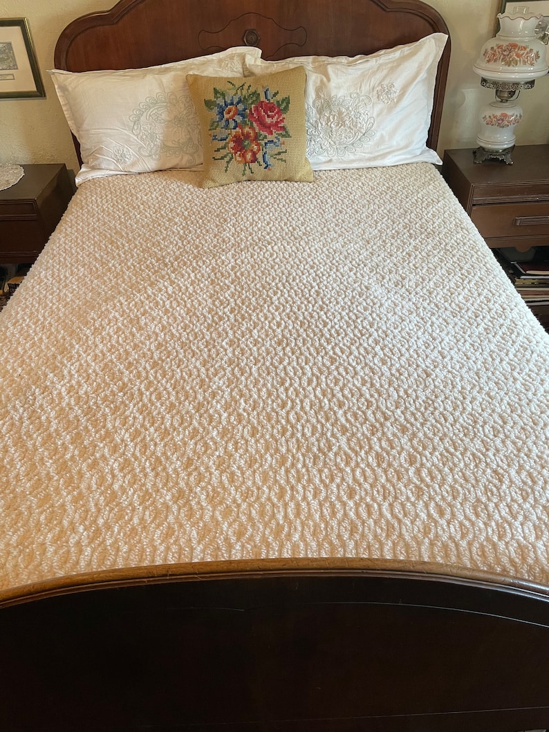 May include: A white tufted bedspread with a floral patterned pillow on a wooden bed frame.