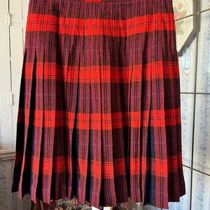 May include: A red and black tartan pleated skirt. The skirt is made from a thick, woven fabric and has a simple, classic design.