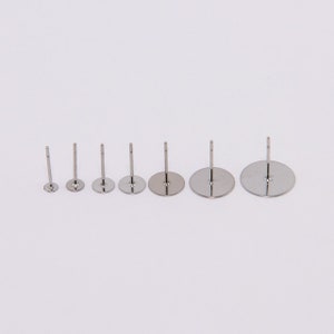 May include: A collection of six silver-colored earring posts in varying sizes. Each post has a flat, circular base and a straight, slender post extending upwards. The bases range from small to large, creating a graduated size effect.