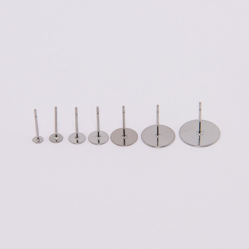 May include: A collection of six silver-colored earring posts in varying sizes. Each post has a flat, circular base and a straight, slender post extending upwards. The bases range from small to large, creating a graduated size effect.