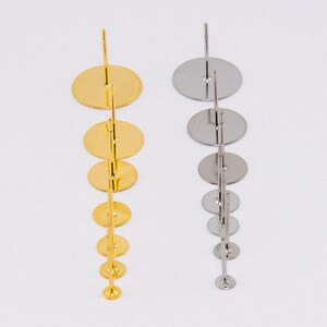 May include: Two earring display stands, one gold and one silver, each with a series of graduated circular platforms. The stands are designed to hold and showcase earrings, with a simple, elegant design.