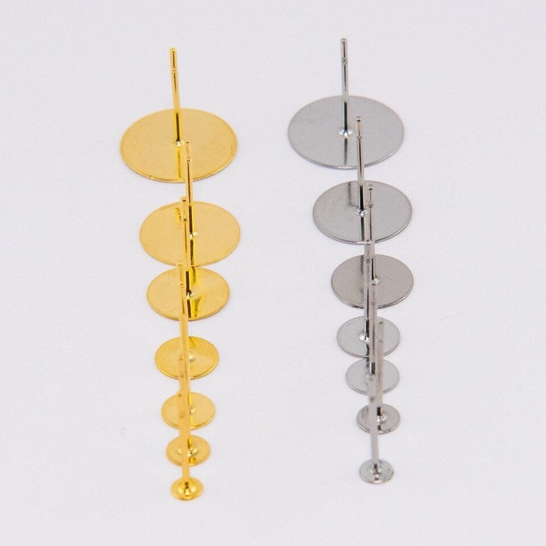 May include: Two earring display stands, one gold and one silver, each with a series of graduated circular platforms. The stands are designed to hold and showcase earrings, with a simple, elegant design.