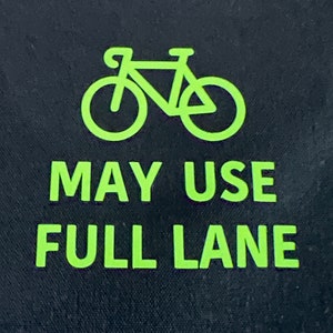 May include: A black and green sign with a white bicycle silhouette and the text "MAY USE FULL LANE".