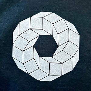 May include: A geometric design featuring a white, three-dimensional, ring-shaped pattern composed of interconnected cubes. The design is set against a dark background, creating a striking contrast. The cubes have a textured appearance.