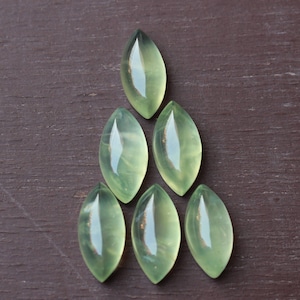 Puede incluir: Siete cabujones de piedra preciosa verde en forma de lágrima dispuestos en un patrón triangular. Las piedras son translúcidas y tienen un ligero brillo.