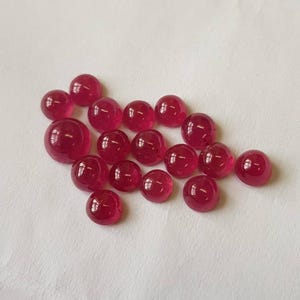 May include: A collection of 17 round, red ruby cabochons. The cabochons are smooth and polished, with a slight shine.