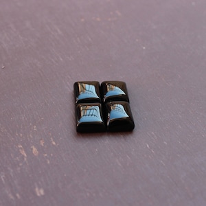 Könnte beinhalten: Vier schwarze quadratische Onyx-Cabochons, jeder mit einer reflektierenden Oberfläche.