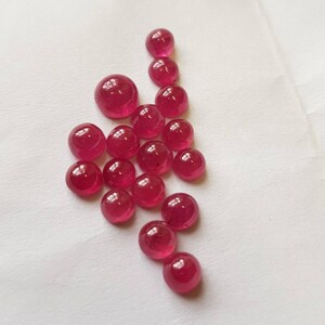 May include: A collection of 18 round, cabochon-cut ruby gemstones. The stones are various sizes and shades of red.